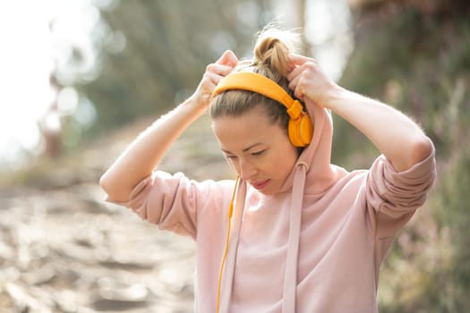 Portrait of beautiful sports woman with hoodie and headphones during outdoors training session. Healthy lifestyle image of young caucasian woman jogging outside.