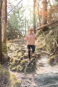 Active sporty woman listening to the music while running in autumn fall forest. Female runner training outdoor. Healthy lifestyle image of young caucasian woman jogging outside.
