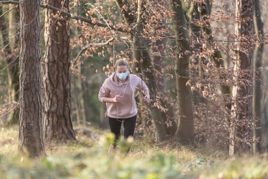 Portrait of caucasian sporty woman wearing a medical protection face mask while running in nature. Corona virus, or Covid-19, is spreading all over the world.