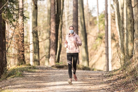 Portrait of caucasian sporty woman wearing a medical protection face mask while running in nature. Corona virus, or Covid-19, is spreading all over the world.