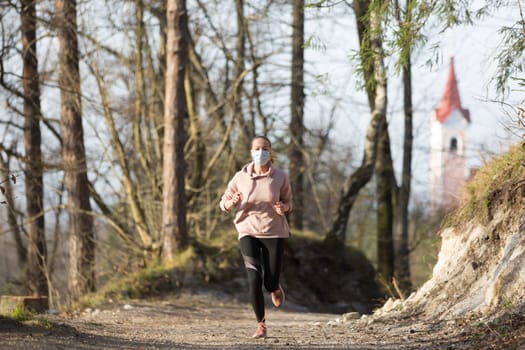 Portrait of caucasian sporty woman wearing a medical protection face mask while running in nature. Corona virus, or Covid-19, is spreading all over the world.