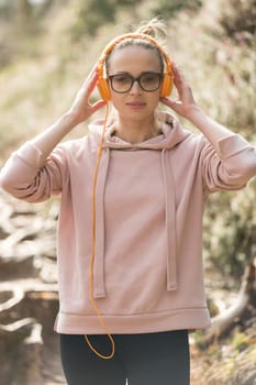 Portrait of beautiful sports woman wearing sunglasses, hoodie and headphones during outdoors training session. Healthy lifestyle image of young caucasian woman jogging outside.