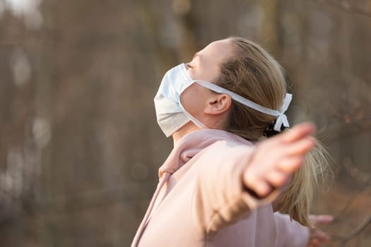 Portrait of caucasian sporty woman wearing medical protection face mask while relaxing by taking a deep breath in nature. Corona virus, or Covid-19, is spreading all over the world.