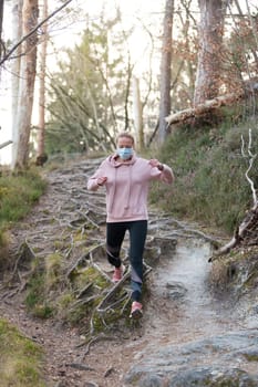 Portrait of caucasian sporty woman wearing a medical protection face mask while running in nature. Corona virus, or Covid-19, is spreading all over the world.