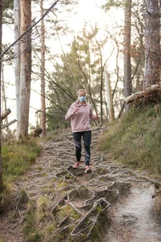 Portrait of caucasian sporty woman wearing a medical protection face mask while running in nature. Corona virus, or Covid-19, is spreading all over the world.