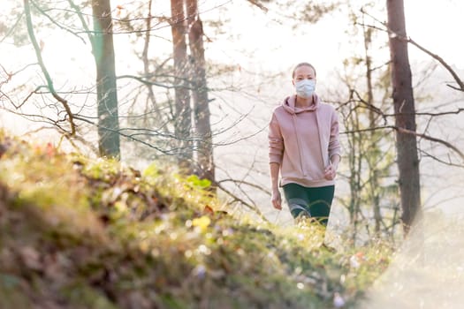 Portrait of caucasian sporty woman wearing a medical protection face mask while walking in the forest. Corona virus, or Covid-19, is spreading all over the world.