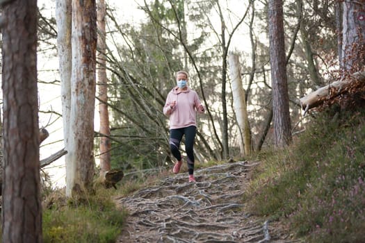 Portrait of caucasian sporty woman wearing a medical protection face mask while running in nature. Corona virus, or Covid-19, is spreading all over the world.