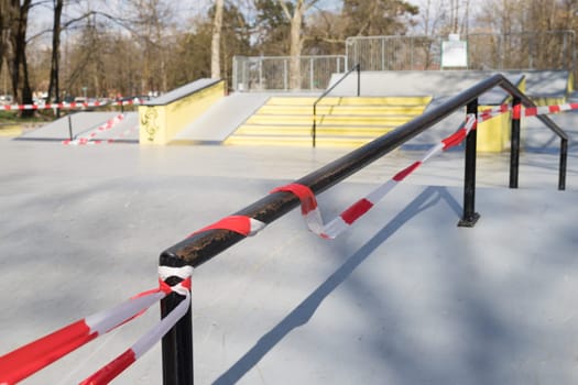 Corona virus COVID-19 restriction. No people due to quarantine. Closed urban skate park. Empty park and playground. Stay at home compaign. Red warning tape on ramps and slides. Social distancing.