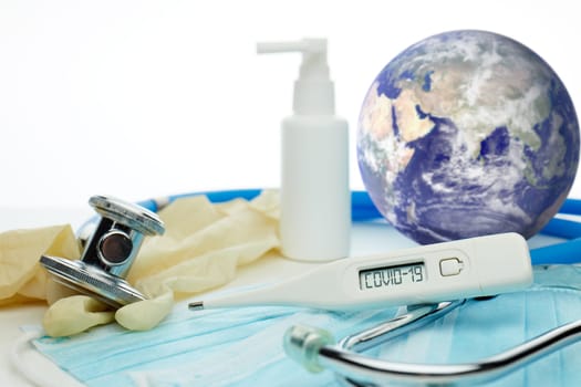 COVID-19. World globe with stethoscope, medical masks, sanitizer, thermometer on white background. Global quarantine,  coronavirus. Elements of this image furnished by NASA. Selective focus on thermometer