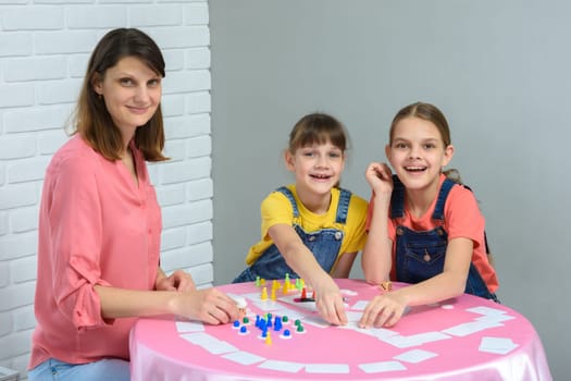 Children and a young mother sit at a table and play a board game