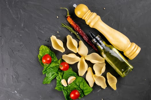 Pasta, big conchiglie and fresh vegetables. Ingredients for italian cuisine, top view. Copy space on black wooden background.