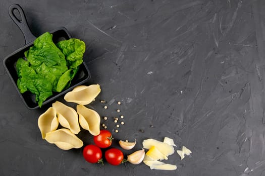 Pasta, big conchiglie and fresh vegetables. Ingredients for italian cuisine, top view. Copy space on black wooden background.