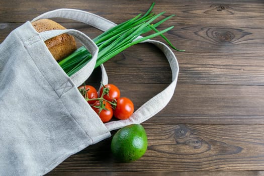 Woven bag of different health food on dark wooden table background. Bread, green onion, garlic, tomato and yellow peper. Top view with clear space.