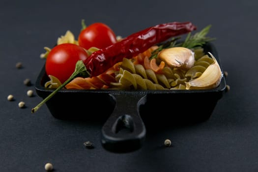 Italian food raw pasta fusilli with tomatoes, rosemary, hot pepper and garlic in a small frying pan. Top views, close-up