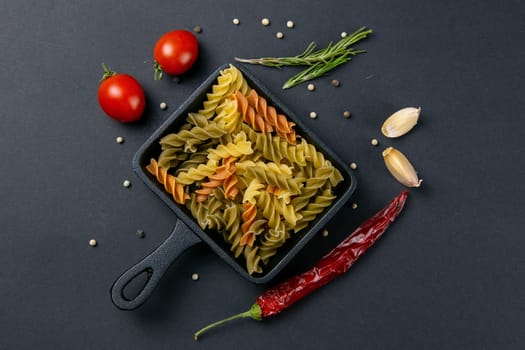 Italian food raw pasta fusilli with tomatoes, rosemary, hot pepper and garlic in a small frying pan. Top views, close-up