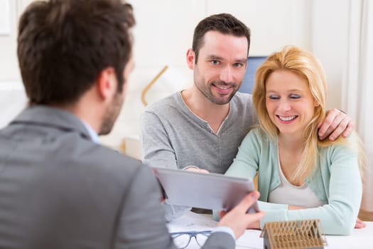 View of a Real estate agent present project on tablet to a young couple
