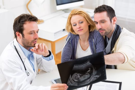 View of a Doctor shows an ultrasound to a young happy couple