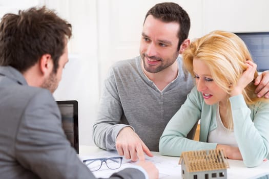 View of a Real estate agent present project on blueprint to a young couple
