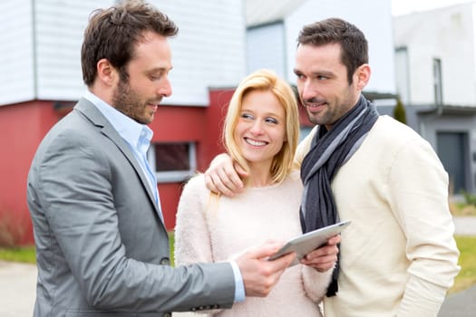 View of a Real estate agent and a young couple in front of their next home