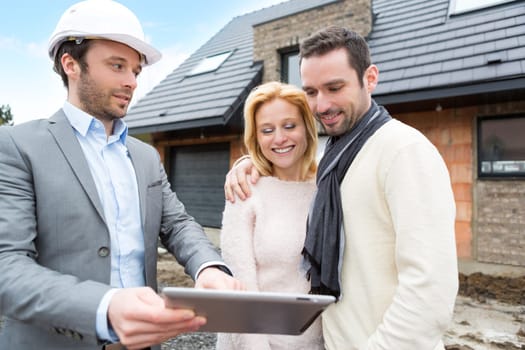 View of a Real estate agent and a young couple in front of future home