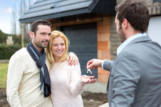 View of a Real estate agent delivers keys to young atractive couple