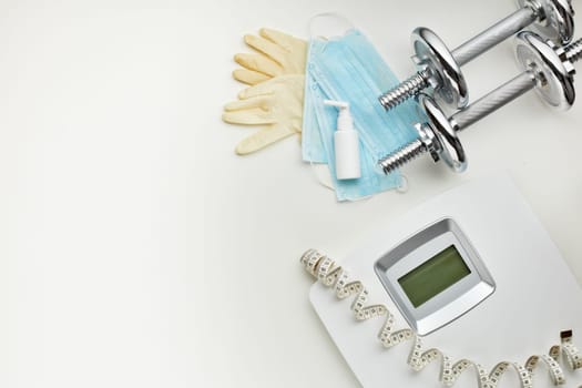 Sport equipment, scales, medical masks and sanitizer on white background. Top view, copy space. Fitness.  Isplation period. Weight and health control during quarantine. Concept of covid or coronavirus