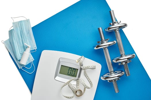 Sport equipment, scales, medical masks and sanitizer on white background. Top view, copy space. Fitness.  Isplation period. Weight and health control during quarantine. Concept of covid or coronavirus
