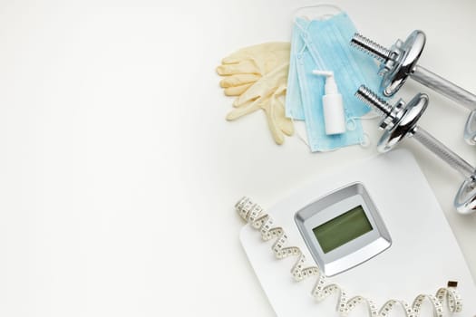Sport equipment, scales, medical masks and sanitizer on white background. Top view, copy space. Fitness.  Isplation period. Weight and health control during quarantine. Concept of covid or coronavirus