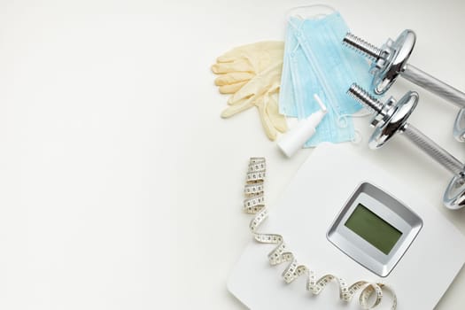Sport equipment, scales, medical masks and sanitizer on white background. Top view, copy space. Fitness.  Isplation period. Weight and health control during quarantine. Concept of covid or coronavirus