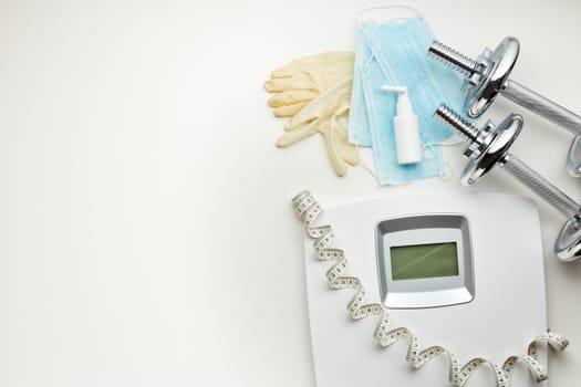 Sport equipment, scales, medical masks and sanitizer on white background. Top view, copy space. Fitness.  Isplation period. Weight and health control during quarantine. Concept of covid or coronavirus