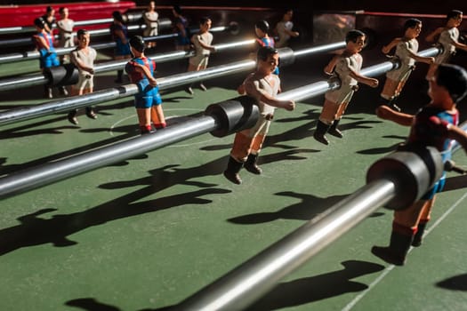 A close-up of an old foosball table with figurines wearing the uniforms of two Spanish teams. In their static nature they metaphorically symbolize the shutdown of the domestic football competitions in Europe due to the spread of the virus throughout the continent. .Side view in detail with selective focus.