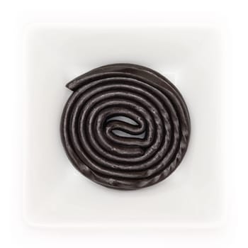 Black licorice wheel in a white bowl in top view