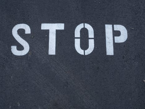 White stop sign painted on dark asphalt. You can see tire tracks over it. Indicates a mandatory stop.