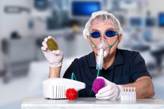 Coronavirus treatment concept. Man at table with nebulizer mask, safety goggles and medical hair hood and gloves shows abstract models of virus covid-19 and ampoules over blurred hospital background.
