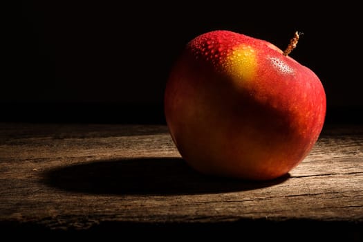 Red apple with water drops on rustic wood in spotlight
