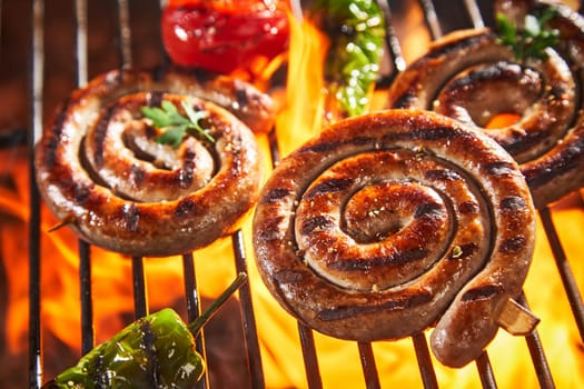 Coils of succulent spicy sausage grilling on a fire at an outdoor barbecue with chili peppers and tomato in close up
