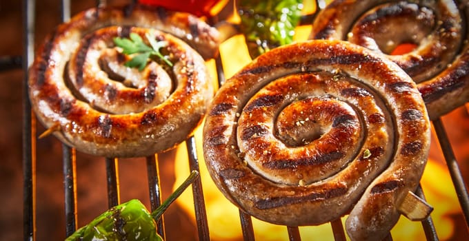 Coils of barbecued sausage on a hot fire grilling over the flames with fresh peppers and tomatoes in a close up view for menu advertising
