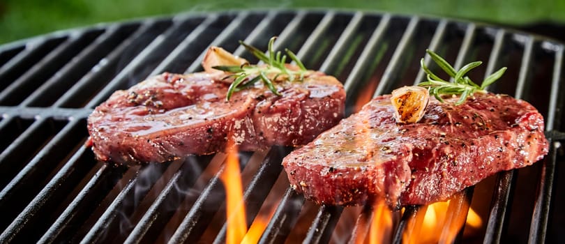 Succulent slices of raw beef steak on a BBQ grilling over the flaming coals in a close up low angle outdoor panorama banner
