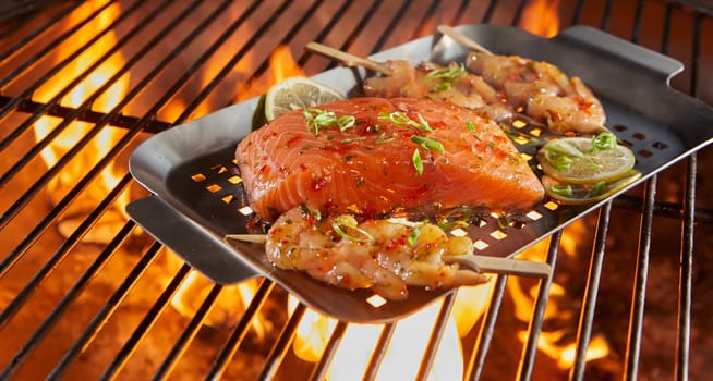 Fresh seafood on a roasting tray over BBQ grill with salmon cutlet and prawns kebabs seasoned with herbs and lemon
