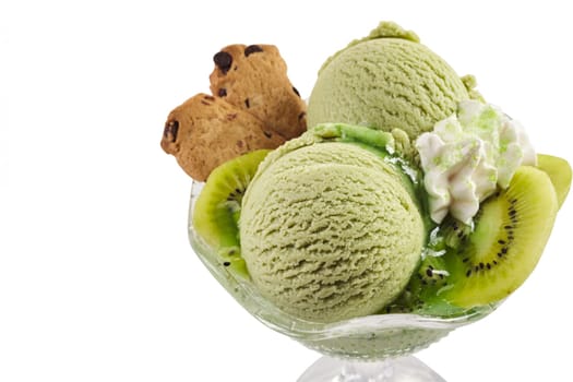 Two scoops of creamy artisanal kiwifruit ice cream with fresh fruit and a dollop of whipped cream garnished with cookies in a glass bowl over white