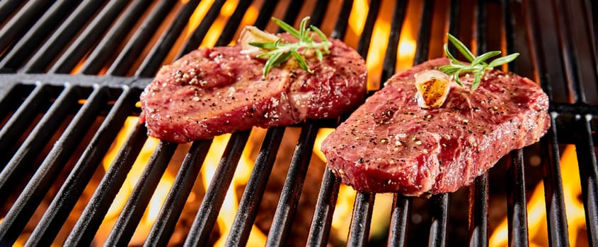 Two portions of raw beef fillet or rump steak seasoned with herbs and spices grilling over a BBQ fire in close up in a panorama banner