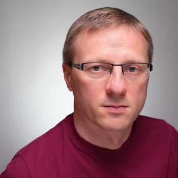 Potrait of a man with glasses and sceptical glimpse grey background..