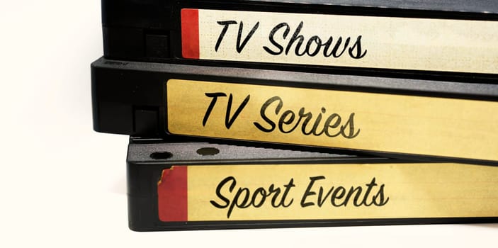 VHS tapes stacked and with labels indicating the various genres of television entertainment recorded on the tape on a white background. Television video recording on cassette. Obsolete video format