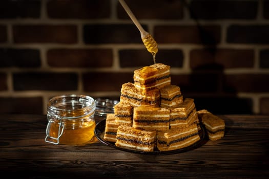 Plate with slices of honey cake and jar with honey on wooden table and brick wall background