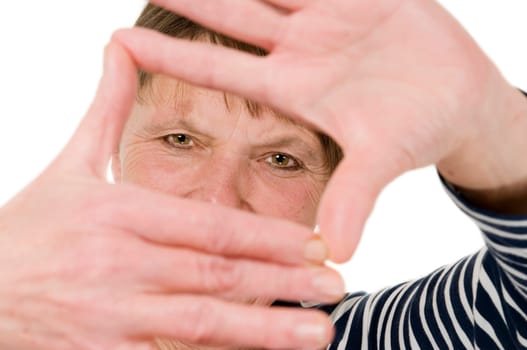 Frontal head and shoulder view of a mature woman holding a hand frame towards the camera against white background.