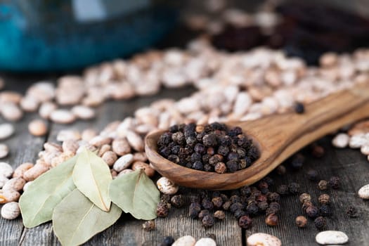 Wooden spoon ful of black peppercorn with pinto beans and bay leaves