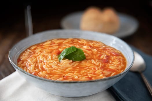 Bowl of orzo pasta and tomato soup with basil