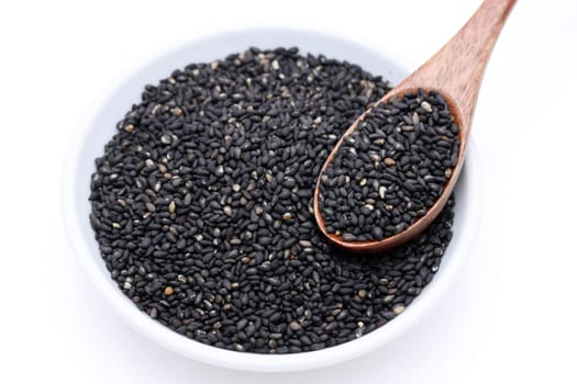 Black sesame seeds with wooden spoon. Sesame seeds in a dish on white background