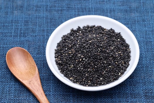 black sesame seeds in a dish with wooden spoon on table