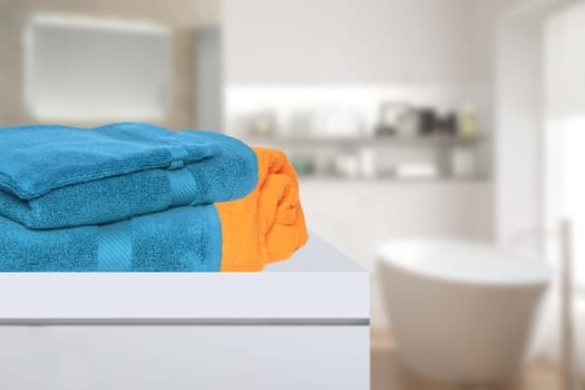 Closeup of a stack or pile of blue and a yellow soft terry bath towels on a table over blurred bathroom background with copy space. For product display montage.